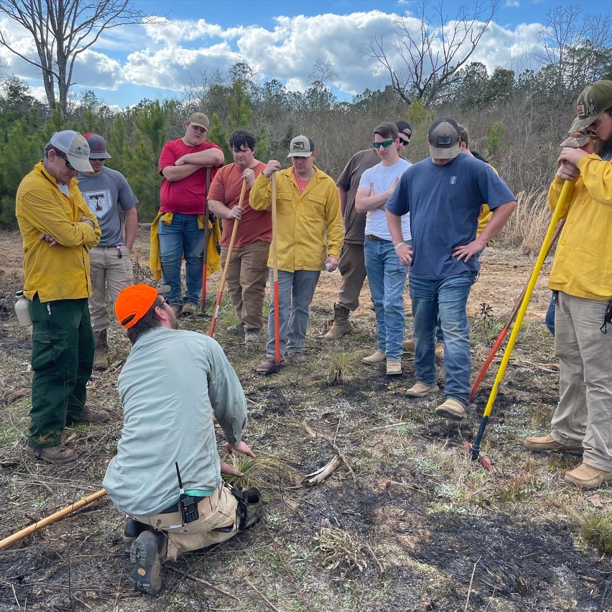 Group of people circled around someone teaching them how to plant. 