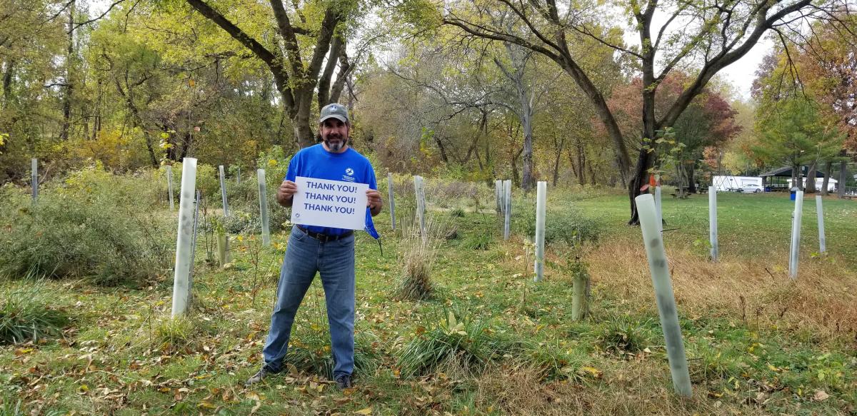 Man holding thank you sign amongst new trees