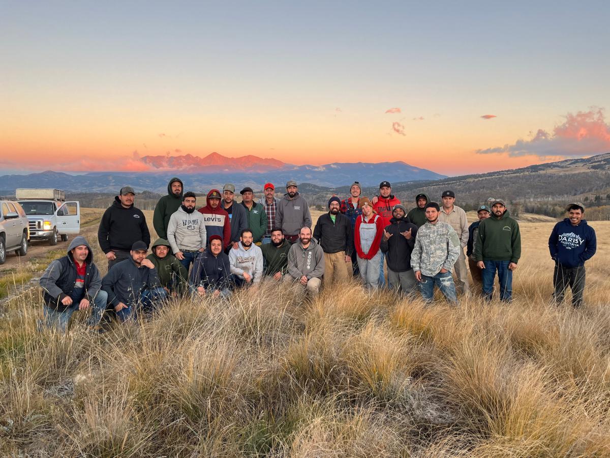 A group of people posing for photo in a grassy field with mountains in the background