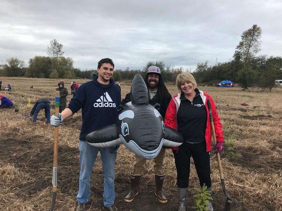 3 people standing in planting field holding an inflatable orca whale and shovels