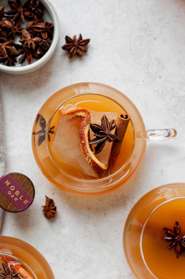 image shows a maple chai cocktail in a glass mug garnished with cinnamon and anise star.
