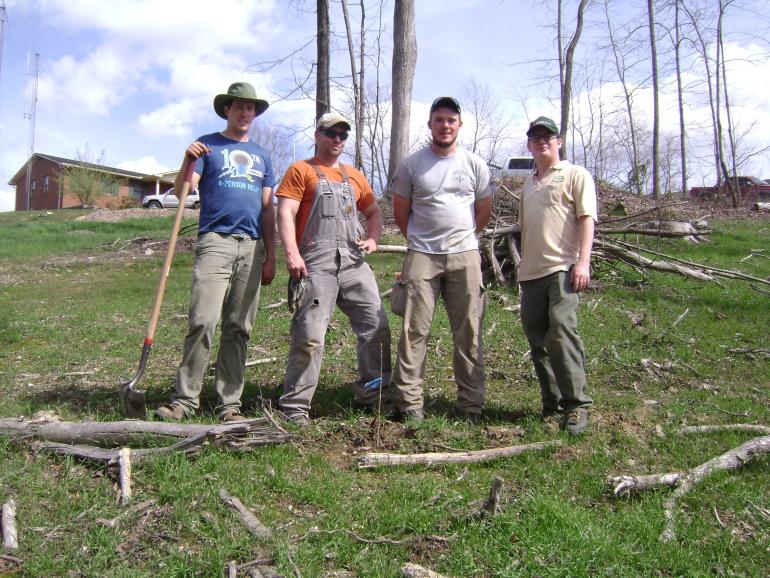 Four Male volunteers stand in field with tools 